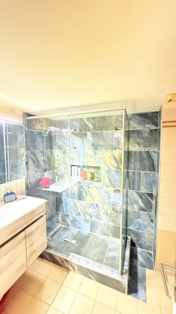 Frameless γυάλινη καμπίνα ντους με ανοιγόμενη πόρτα, μαύρους ματ μεντεσέδες και αντηρίδα, διάφανο κρύσταλλο ασφαλείας, τοποθετημένη σε μπάνιο με μάρμαρο calacatta. Custom κατασκευή DNglass.